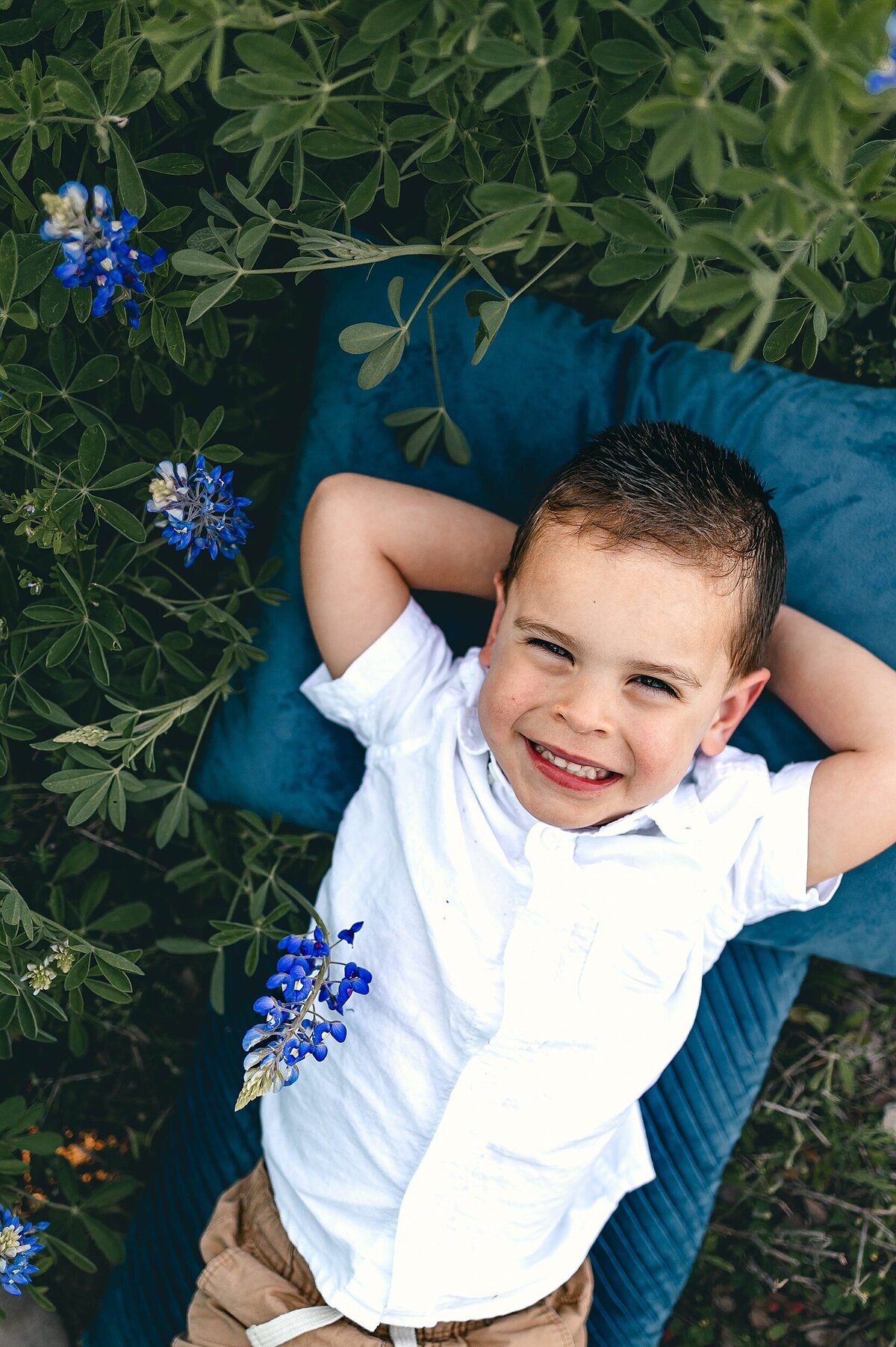 little boy staring up at camera laying on his back in bluebonnets by Cypress Family Photographer