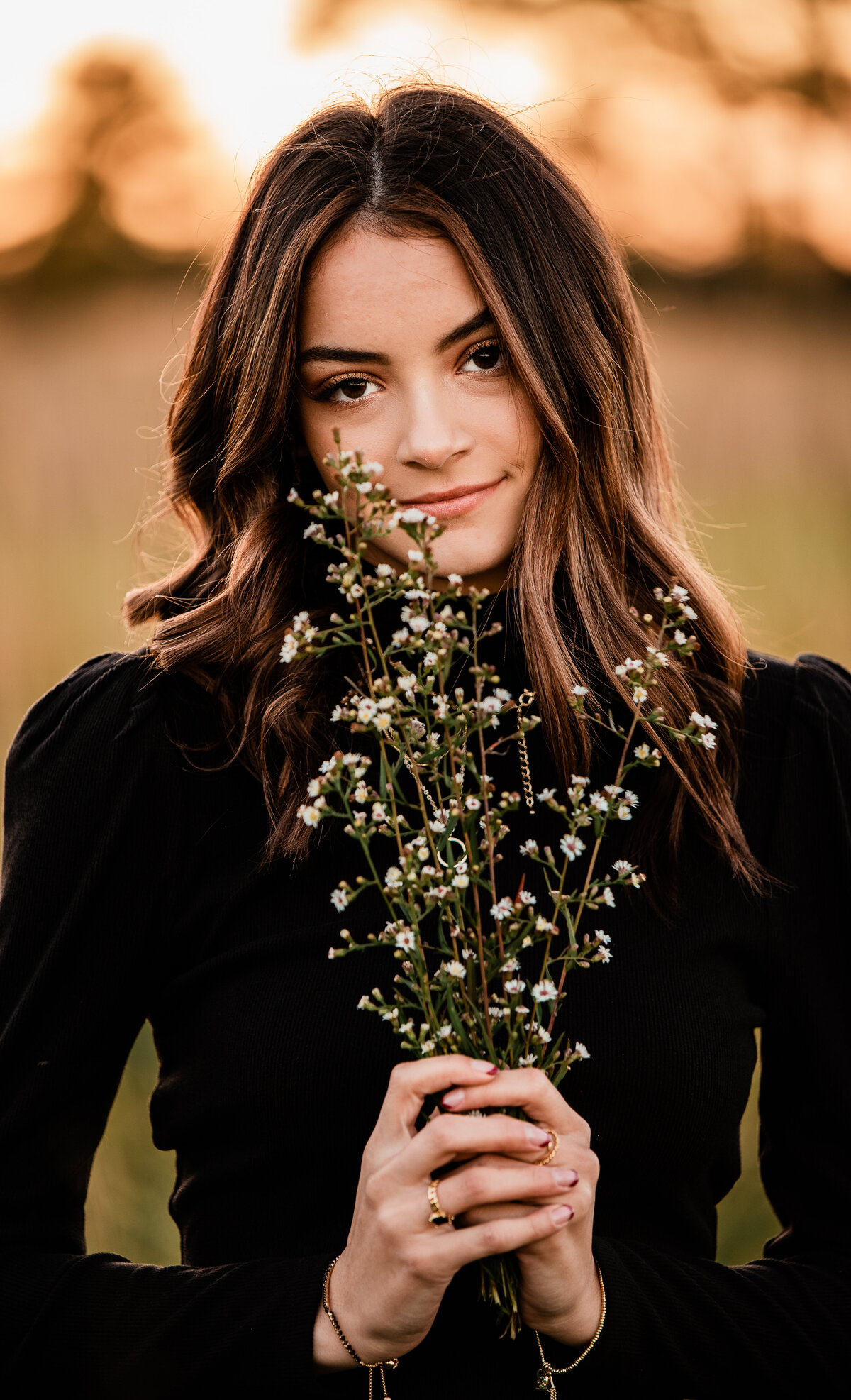 A high school senior wearing a black turtleneck holds wildflowers to her face while looking at the camera.