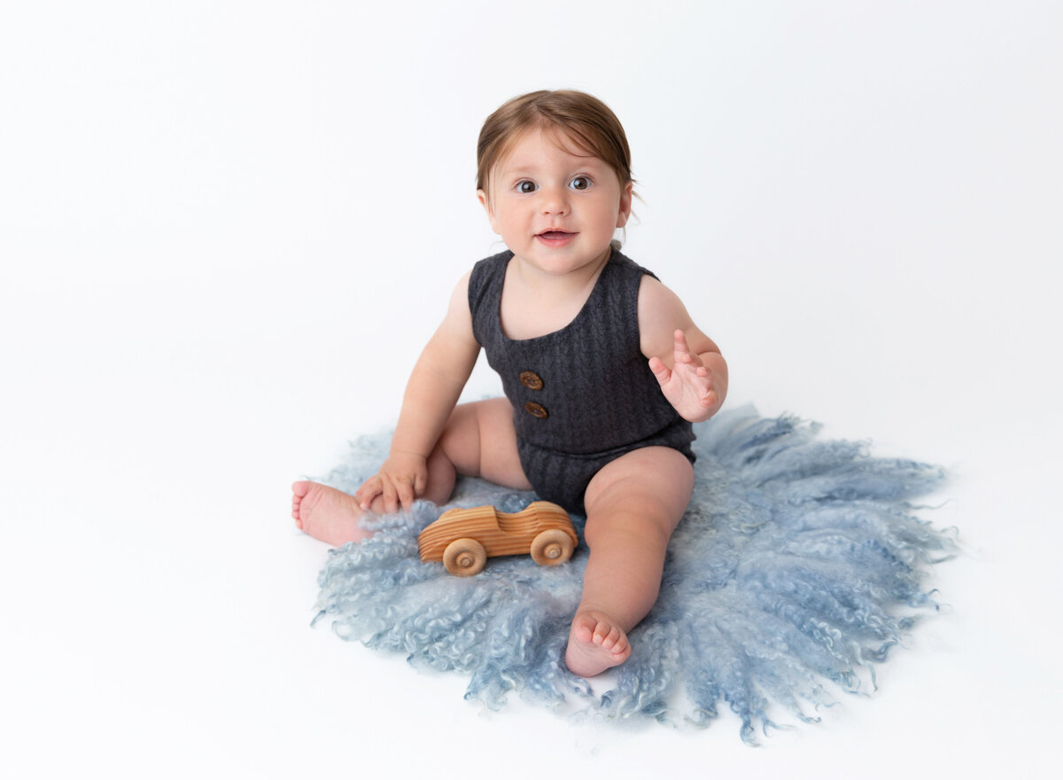 6-month old baby boy sitting for a milestone photoshoot. Baby is sitting on a blue fuzzy rug and smiling at the camera.