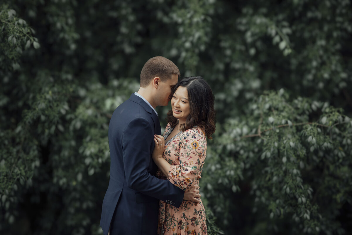 Couple by green bush during spring engagement photo at Fairmount Park Horticulture Center in Philadelphia Pennsylvania