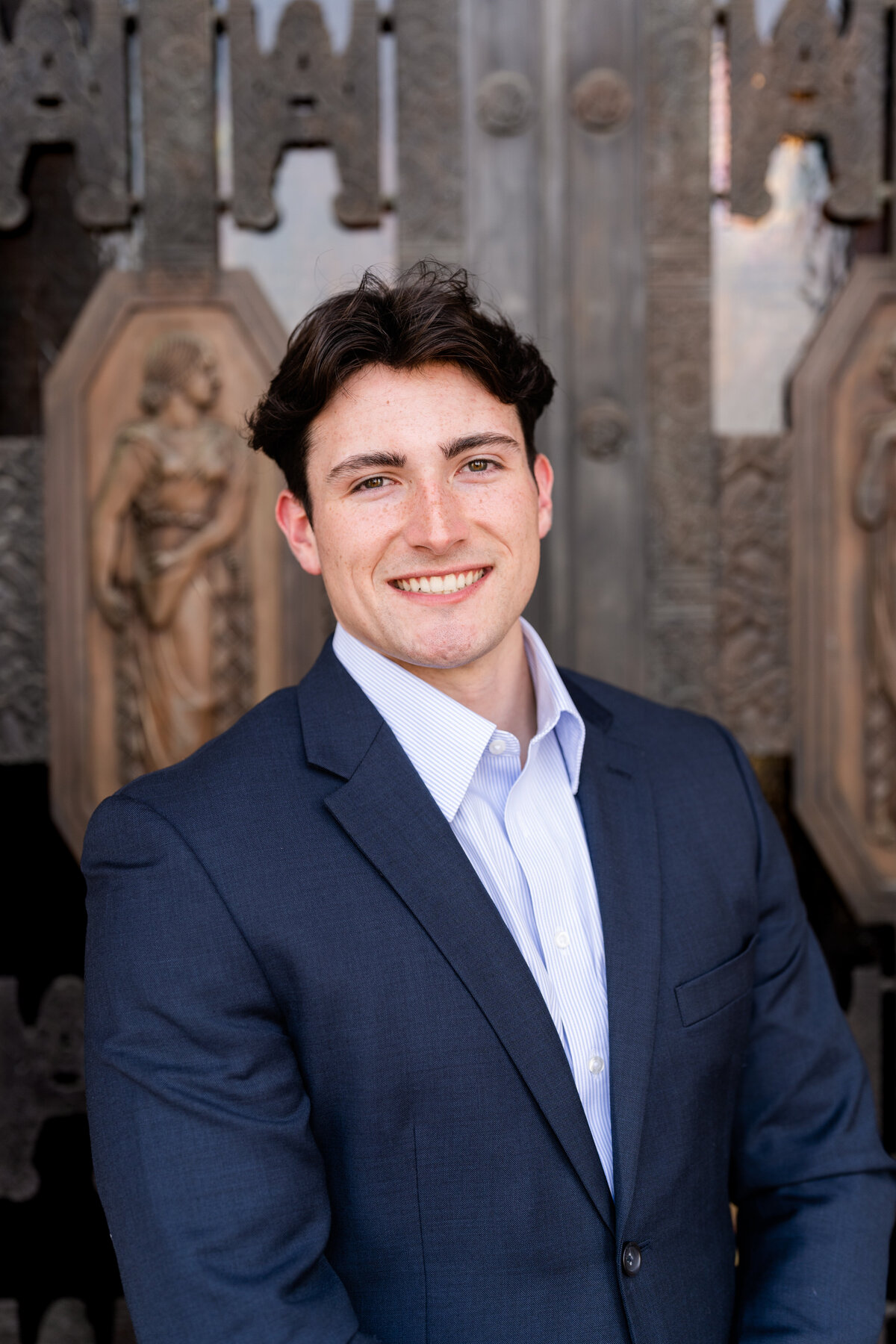 Texas A&M senior guy smiling while wearing a buttoned suit in front of Administration Building front doors