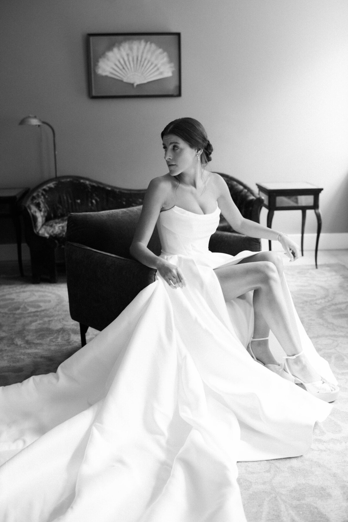 the bride sitting elegantly on a velvet chair, her wedding dress cascading onto the floor