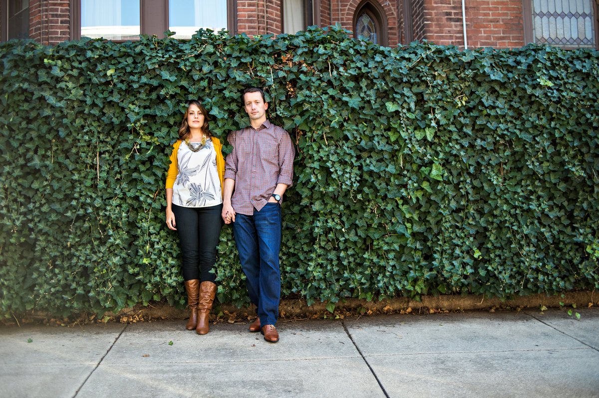 A couple hold hands in front of a wall covered with vines.