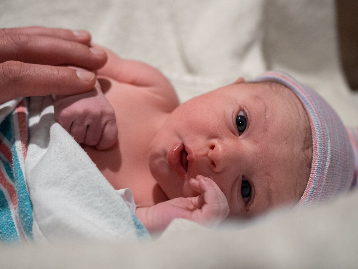 a close up image of a newborn with wide eyes and mouth open as she roots for her mother.