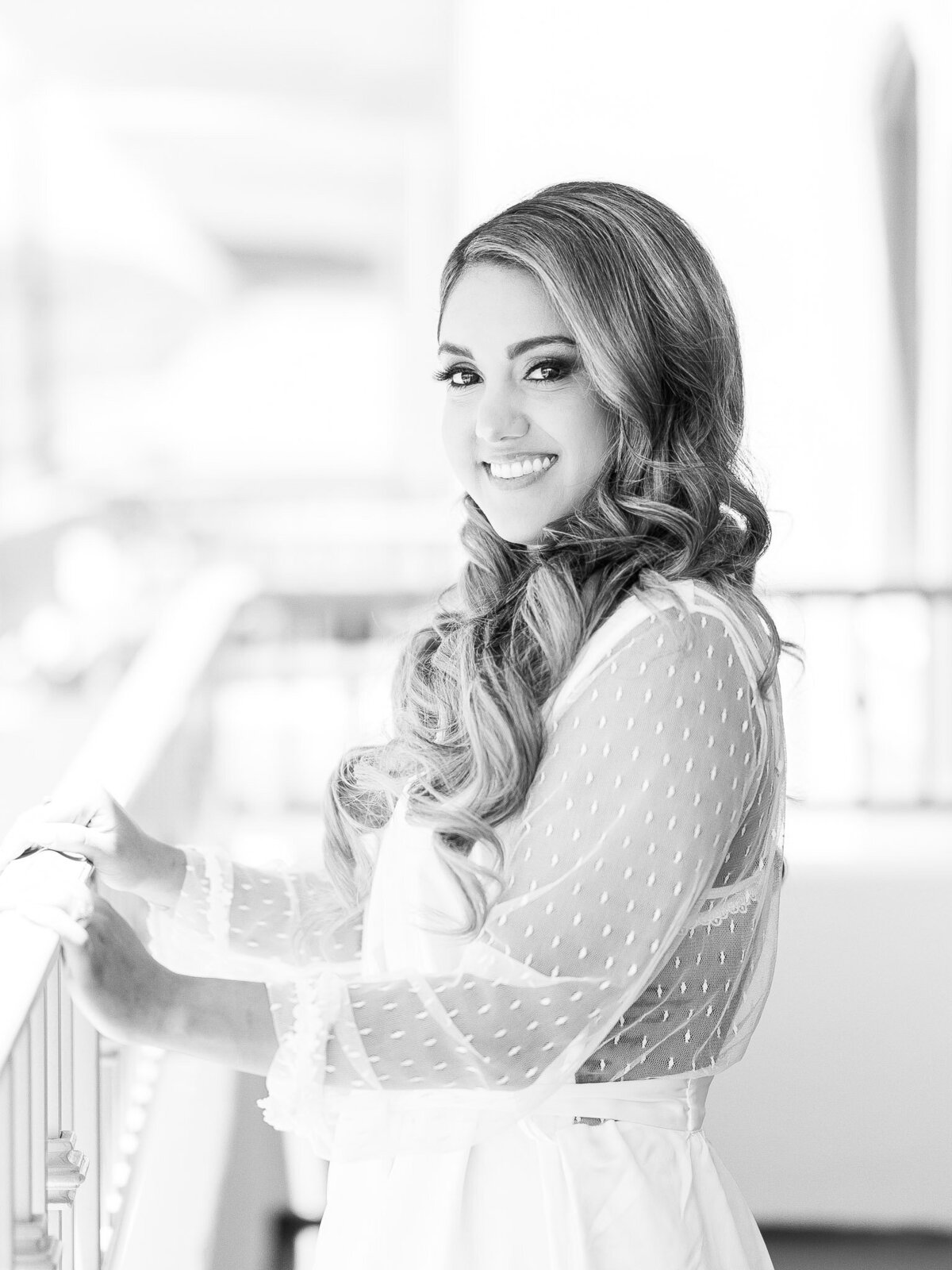 A radiant bride with soft curls and a delicate lace robe smiles as she prepares for her wedding day at the Ritz-Carlton Laguna Niguel
