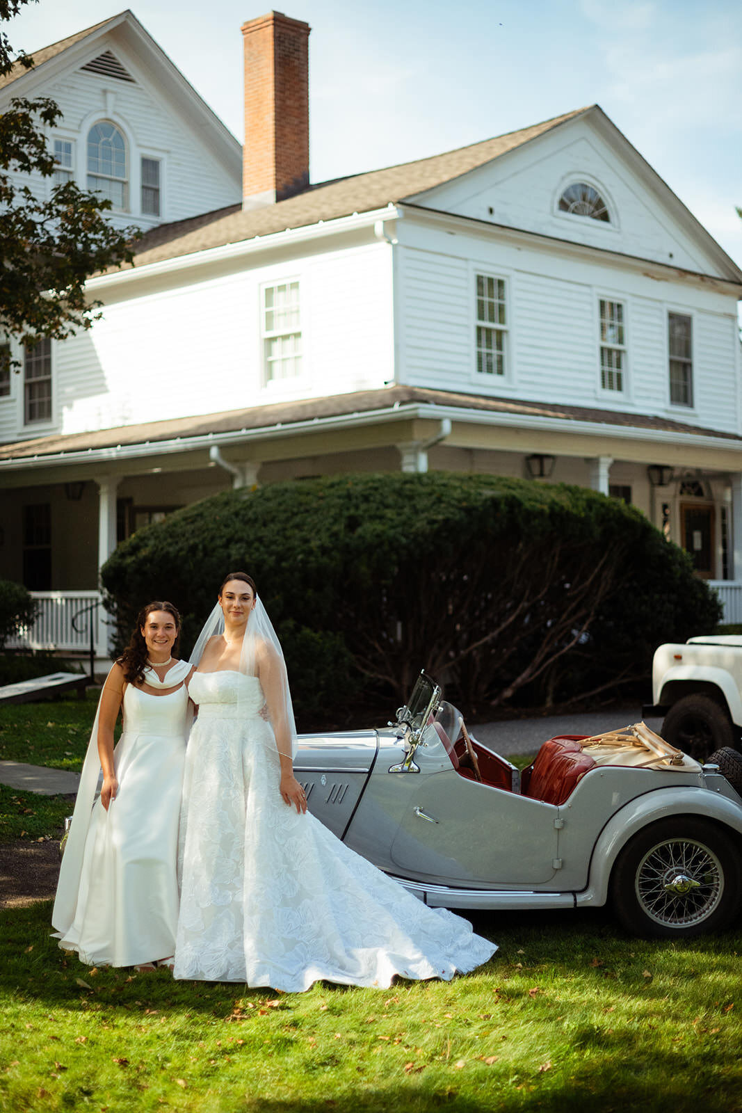 Two brides standing in front of sage vintage car
