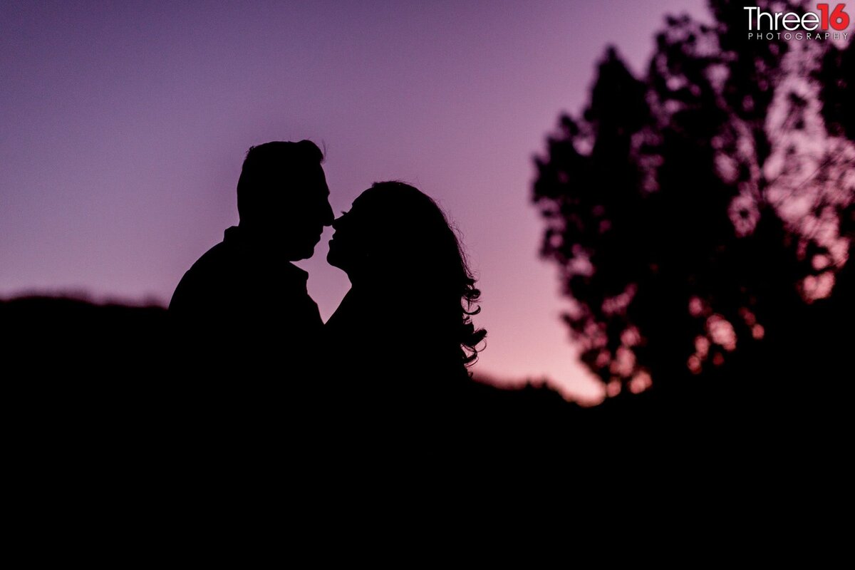 Silhouette of engaged couple about to share a kiss at night