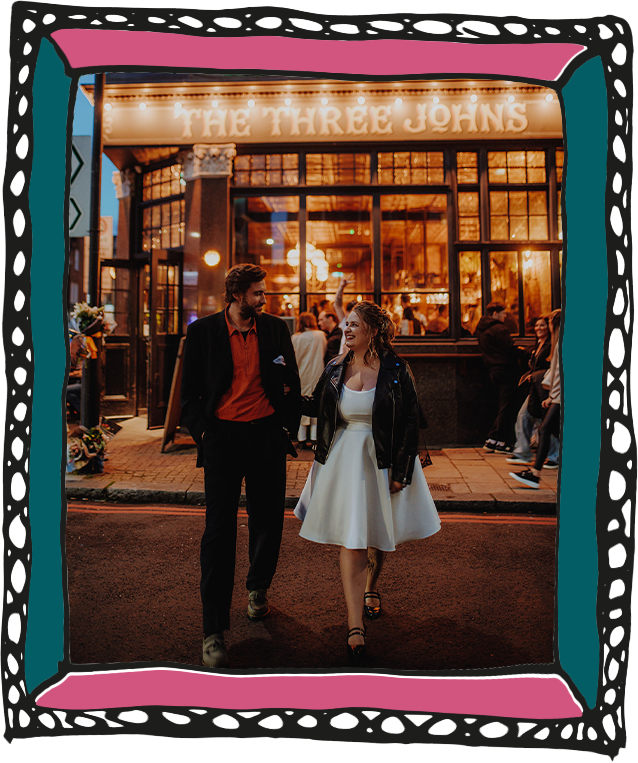 Wedding couple outside The Three Johns, bride in white knee length dress and leather jacket. Groom in dark suit with red shirt.