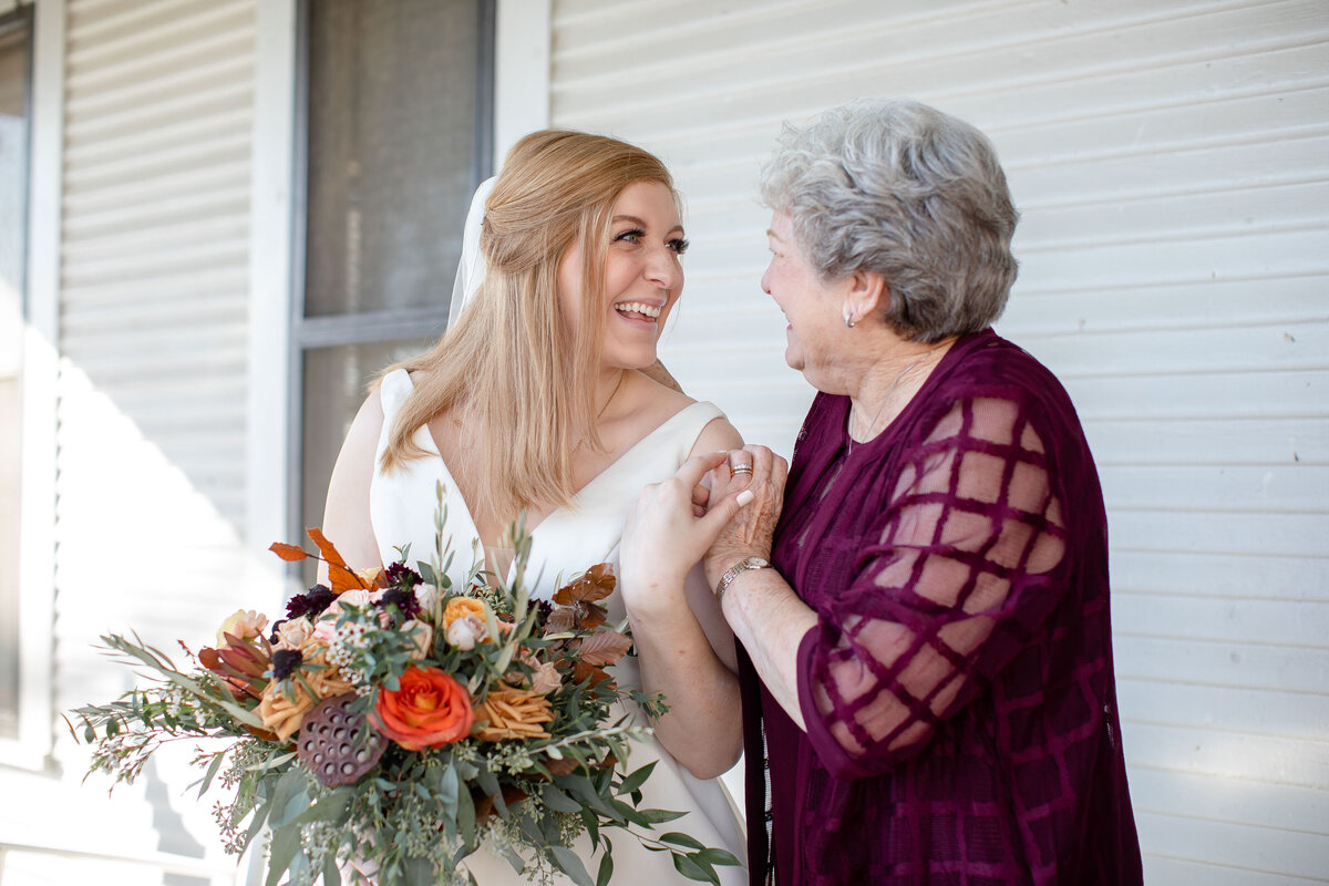 bride embraces grandmother in maroon dress on porch of Allen Farmhaus in New Braunfels Texas