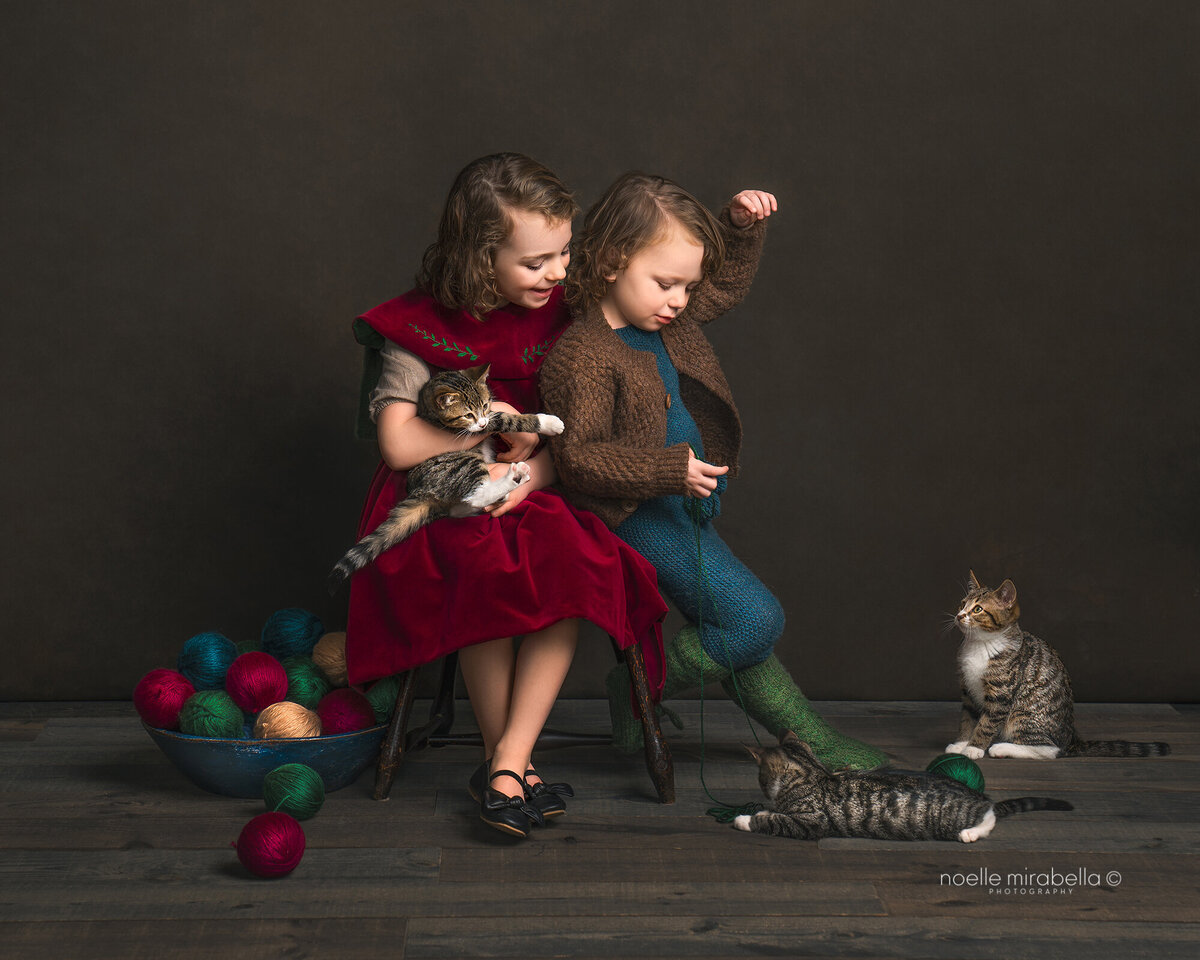 Children wearing vintage style clothing playing with kittens and yarn.