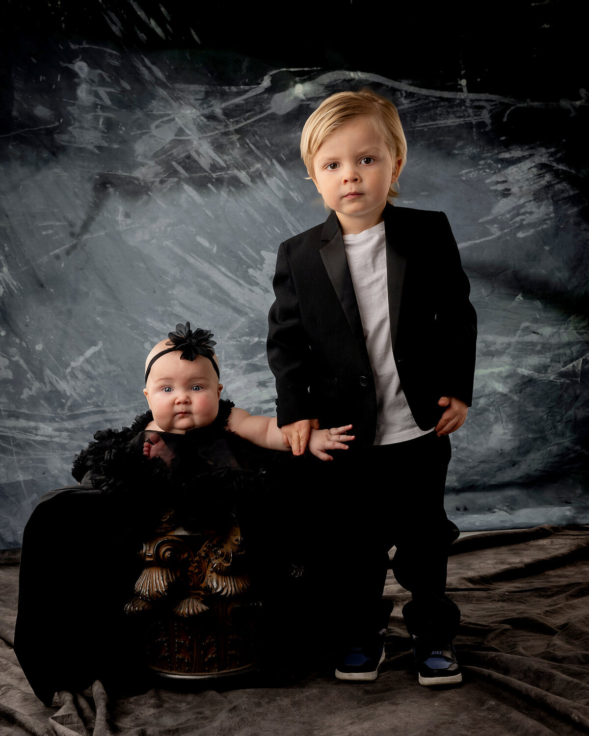 Brother stands and holds hands with his sitting sister with serious expressions