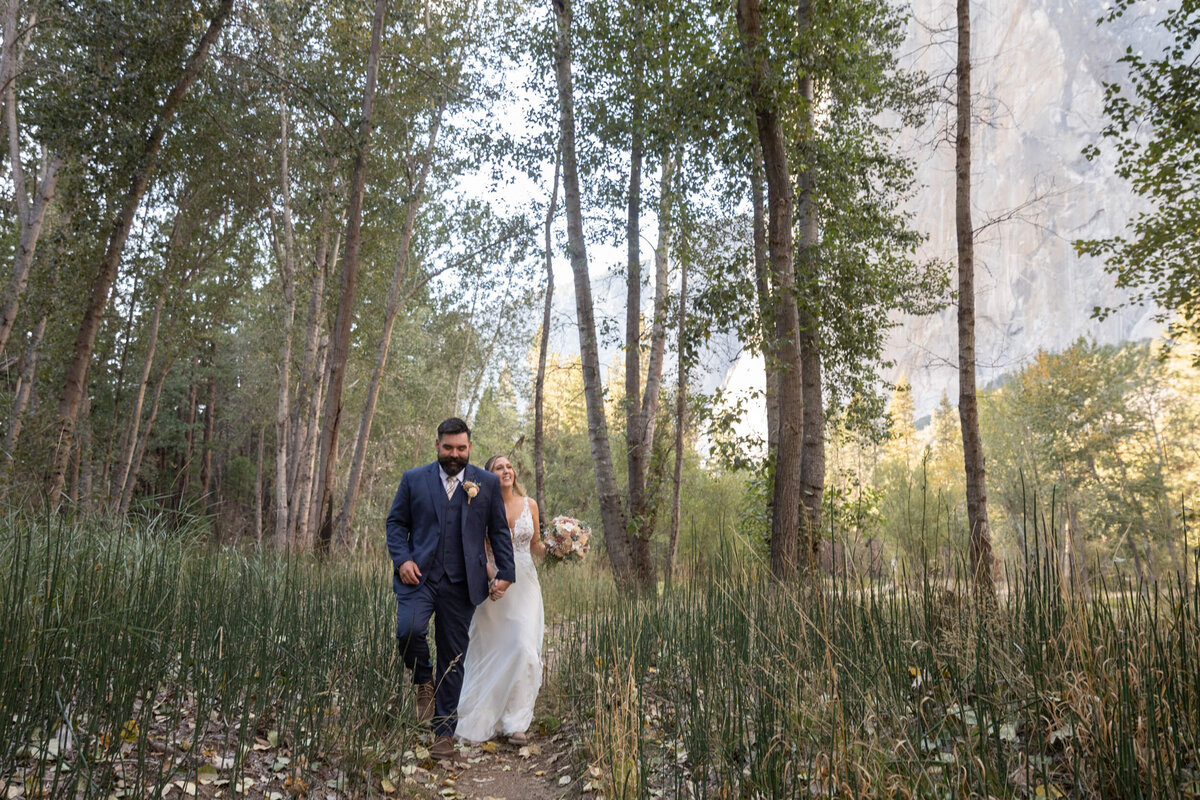 A bride and groom walk through a grassy meadow in Yosemite.
