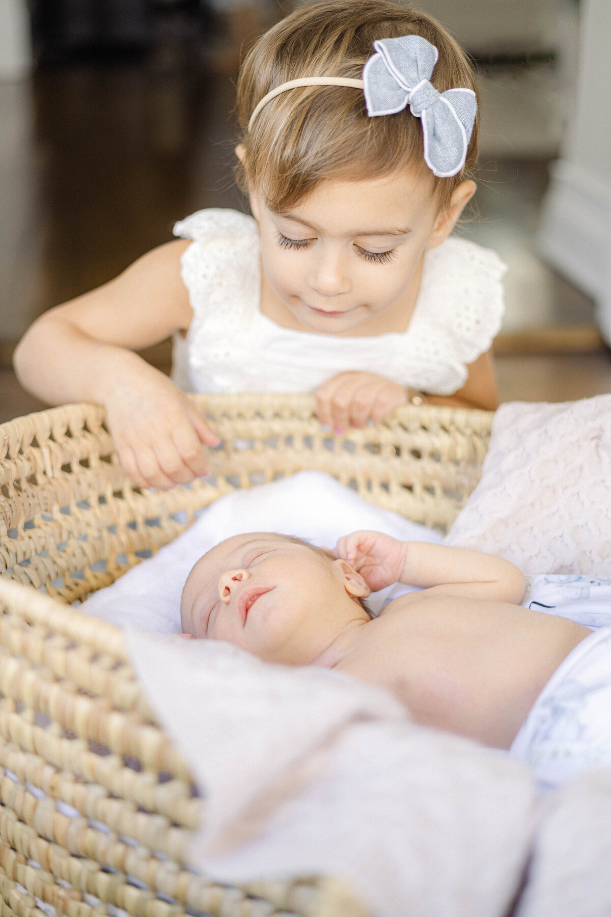 Tender moment of big sister watching over her newborn brother in the bassinet.