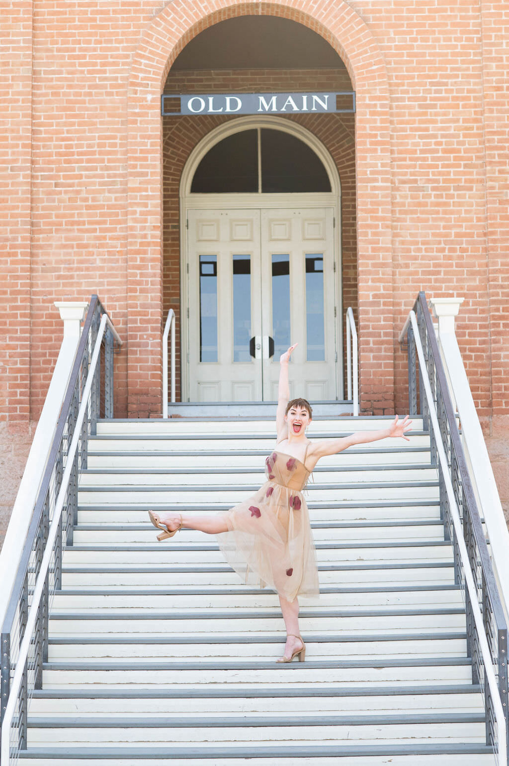 A girl with one leg kicked out and her arms outstretched while standing on a staircase.