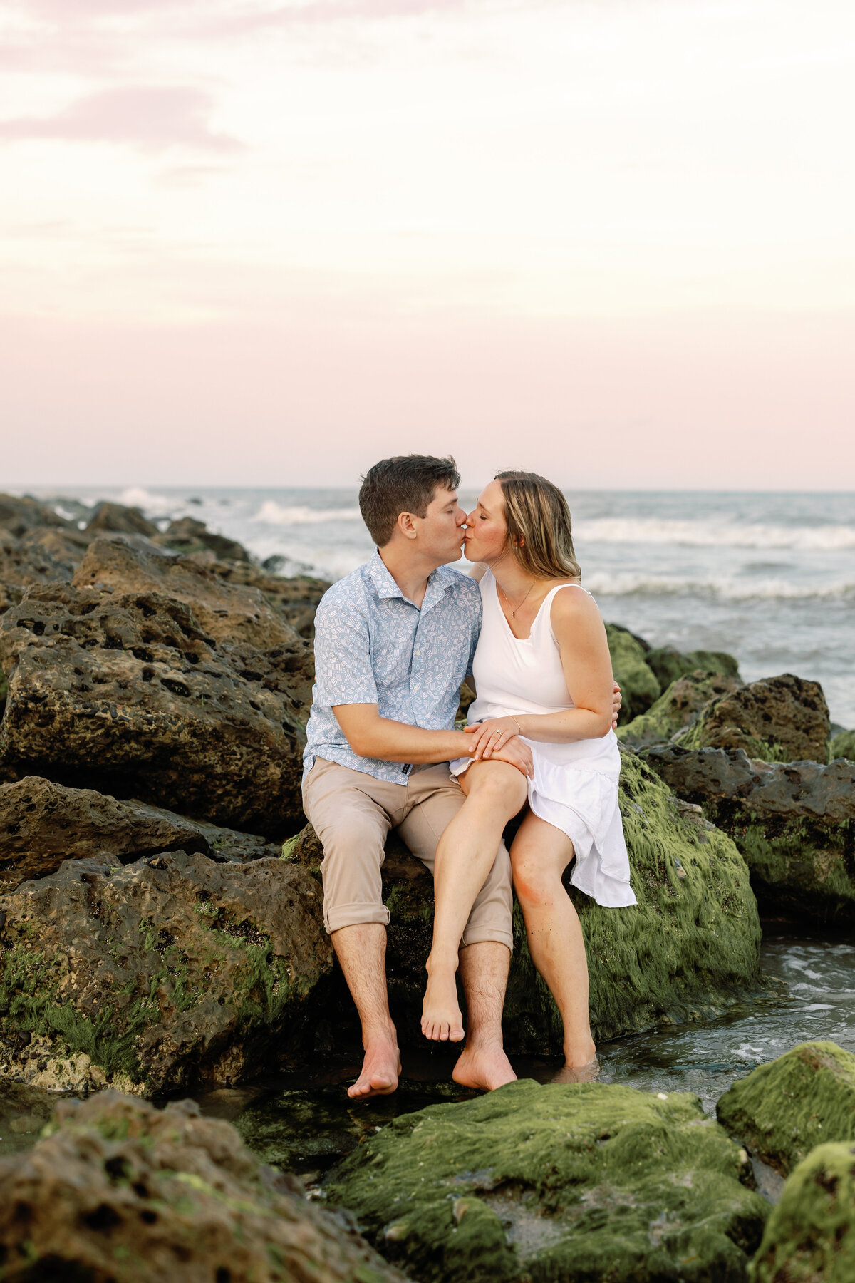 Couple kissing while sitting on large rock, picturesque Wilmington beach backdrop