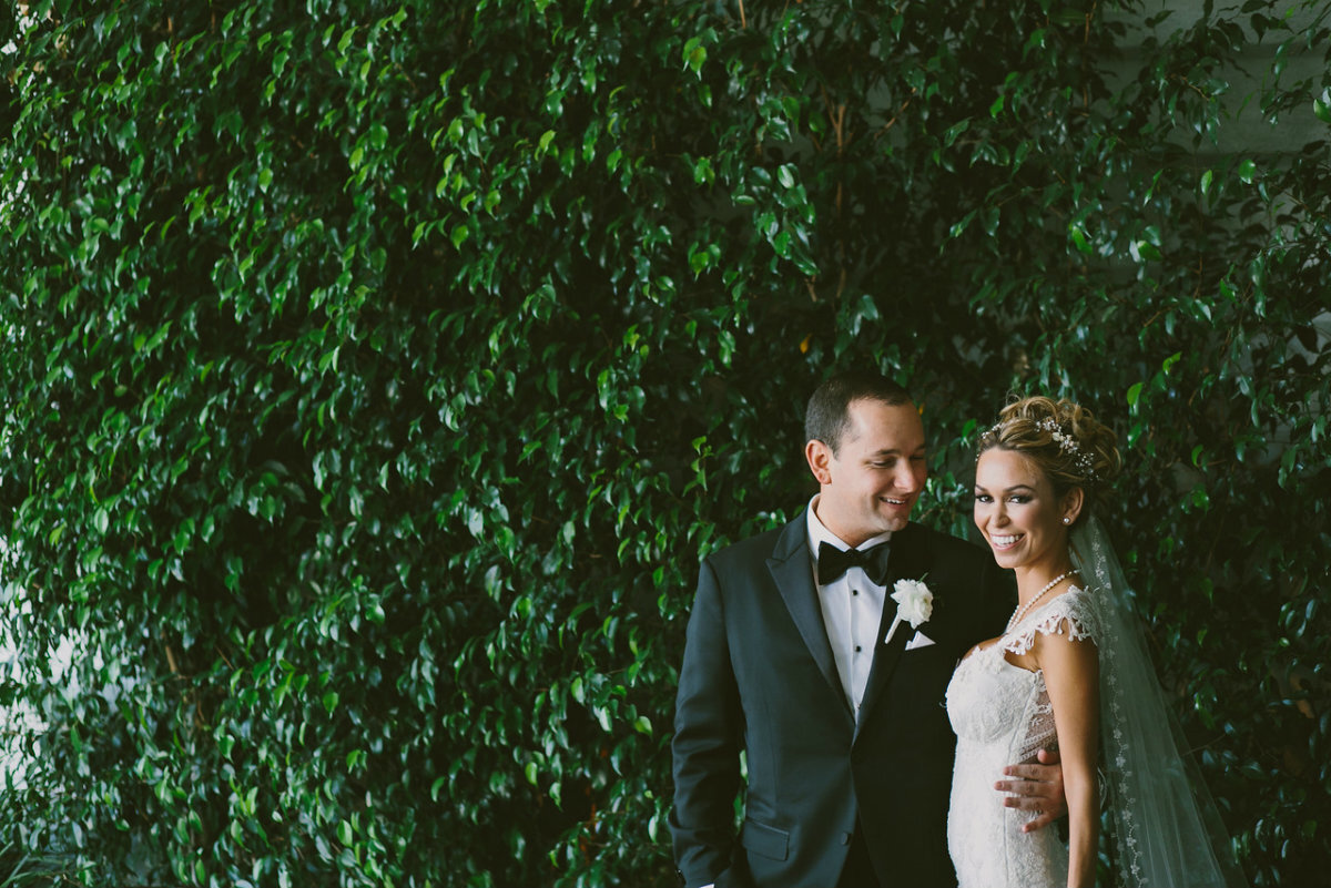 bride and groom standing in front of hedge wall