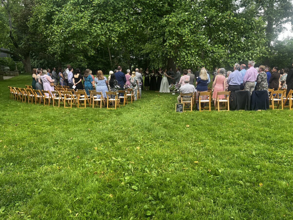 wooden chairs set up on two sides of an aisle with guests viewing a wedding ceremony