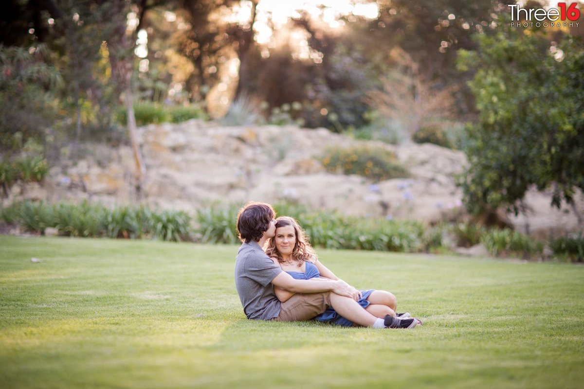Engaged couple cuddle up on the grassy area of UC Irvine