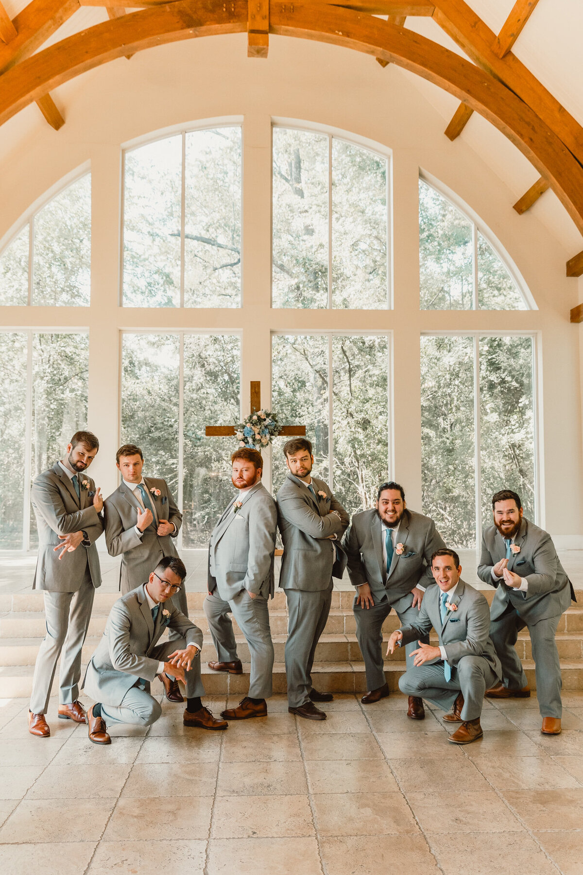 Groomsmen group portrait taken at Ashton Gardens North in Houston, Texas. The groomsmen are dressed in matching gray suits, posing with confidence in front of the grand window backdrop. Captured during Zach and Emily’s wedding by ShutterUp Photography.