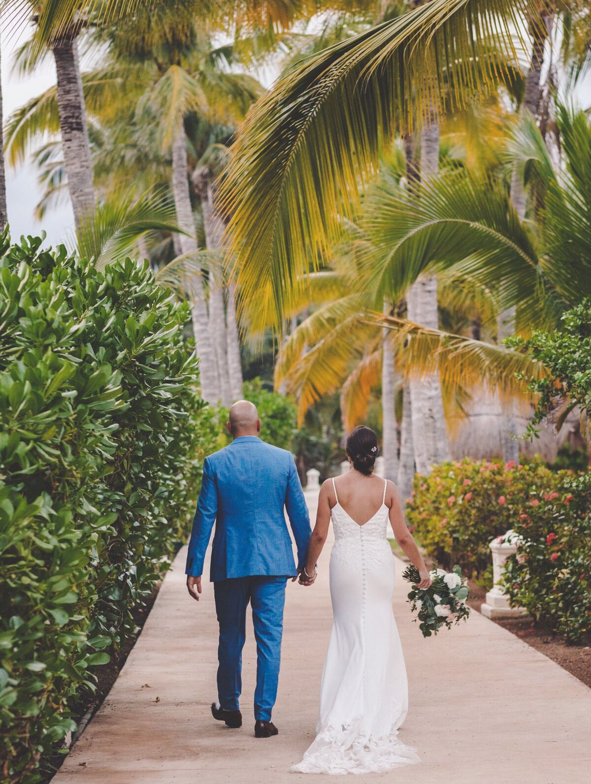 Bride and groom walking away on path with palm trees at wedding in Riviera Maya