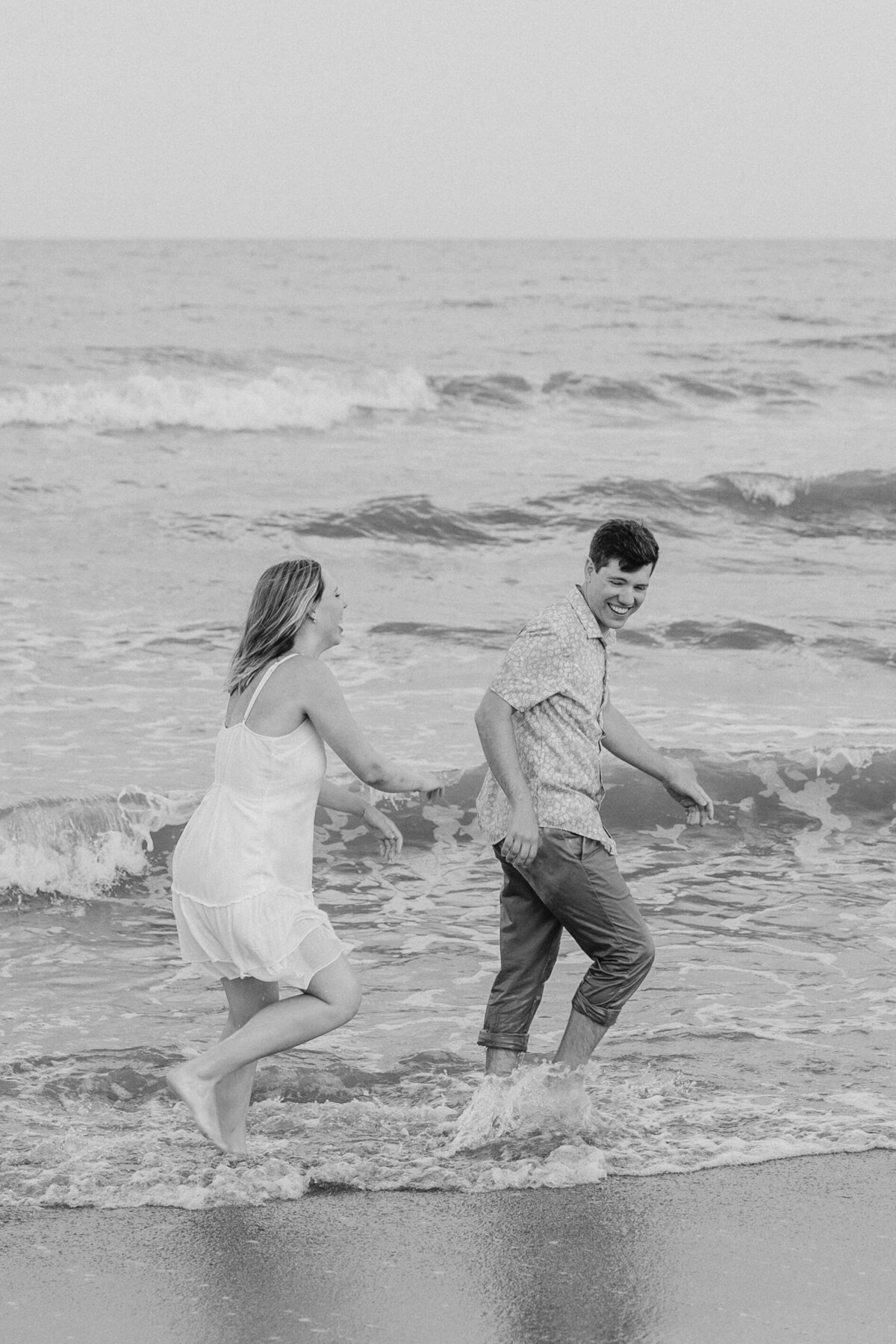 Couple running through water, creating splashes on Wilmington beach, fun engagement photo