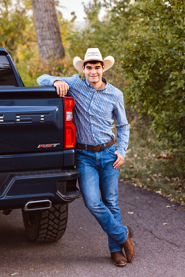 Boy with cowboy hat leans on black truck.