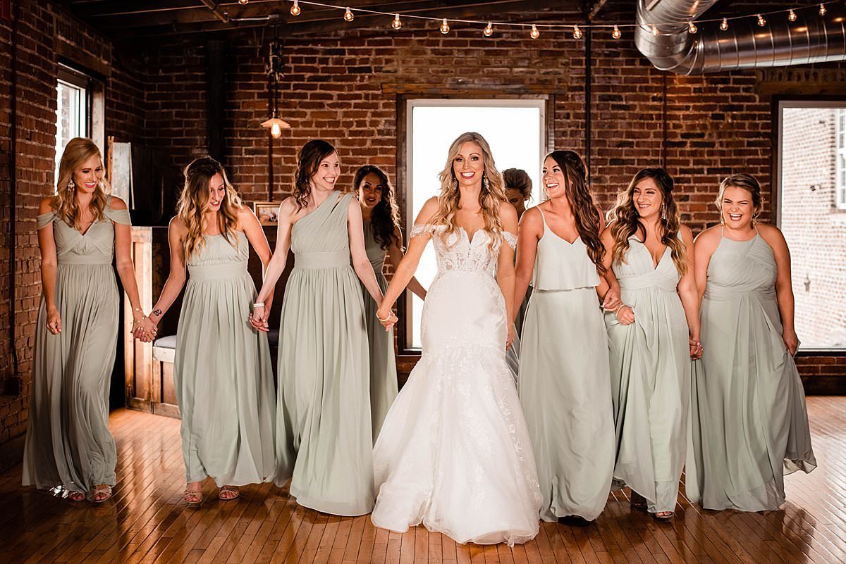 All the ladies in the wedding party holding hands and walking together inside of Cannery ONE