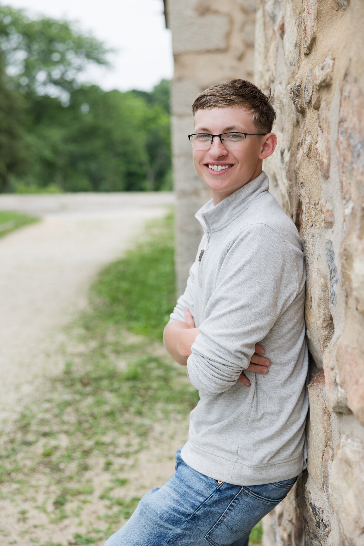 Senior guy leaning against a rock wall smiling at the camera