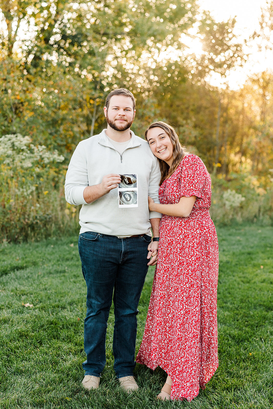 Pregnant couple standing outside holding sonogram images