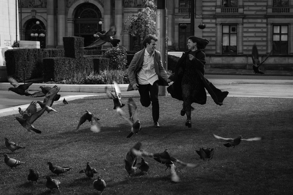 Two young lovers run romantically through a city. the nearby pigeons scatter