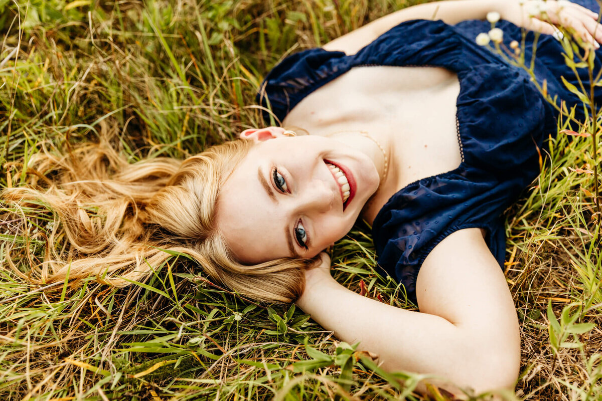 beautiful close up of a high school senior girl laying down in grass and smiling captured by Ashley Kalbus Photography
