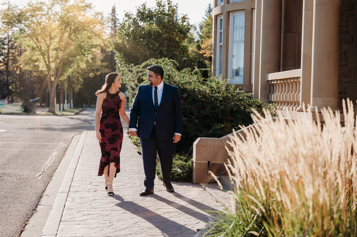 couple walking down sidewalk in front of historical building, holding hands and smiling