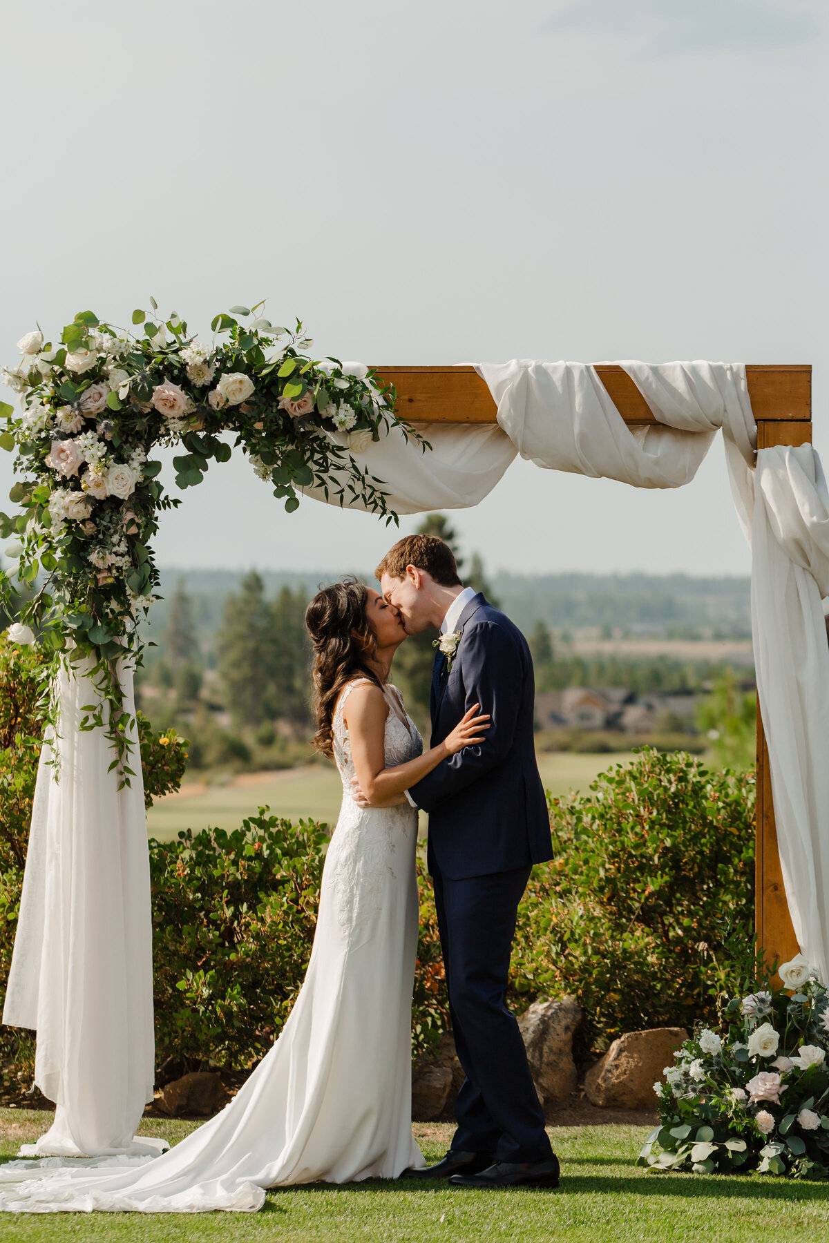 Wedding ceremony with white and blush roses and greenery on square wooden arch with fabric draping at Tetherow Resort in Bend