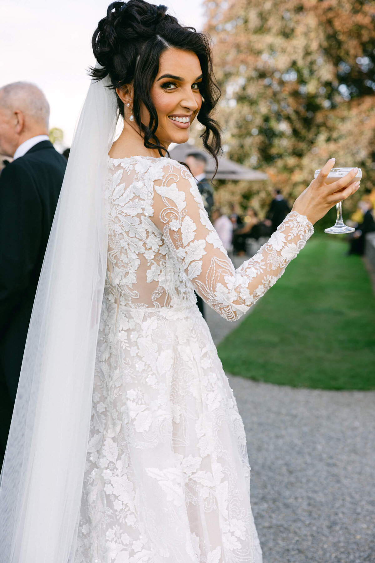 A wedding day photo of the bride in her white dress holding her cocktail smiling at the camera at her wedding at Luttrellstown Castle