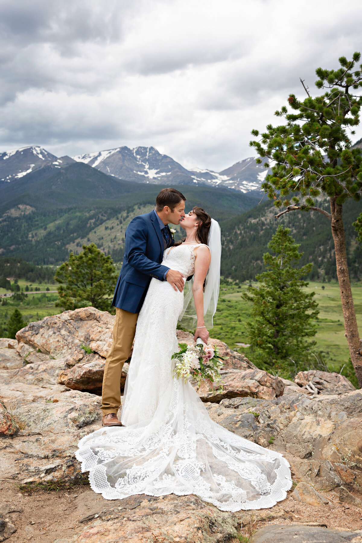 groom in navy and tan dips his bride with the mountains in the background