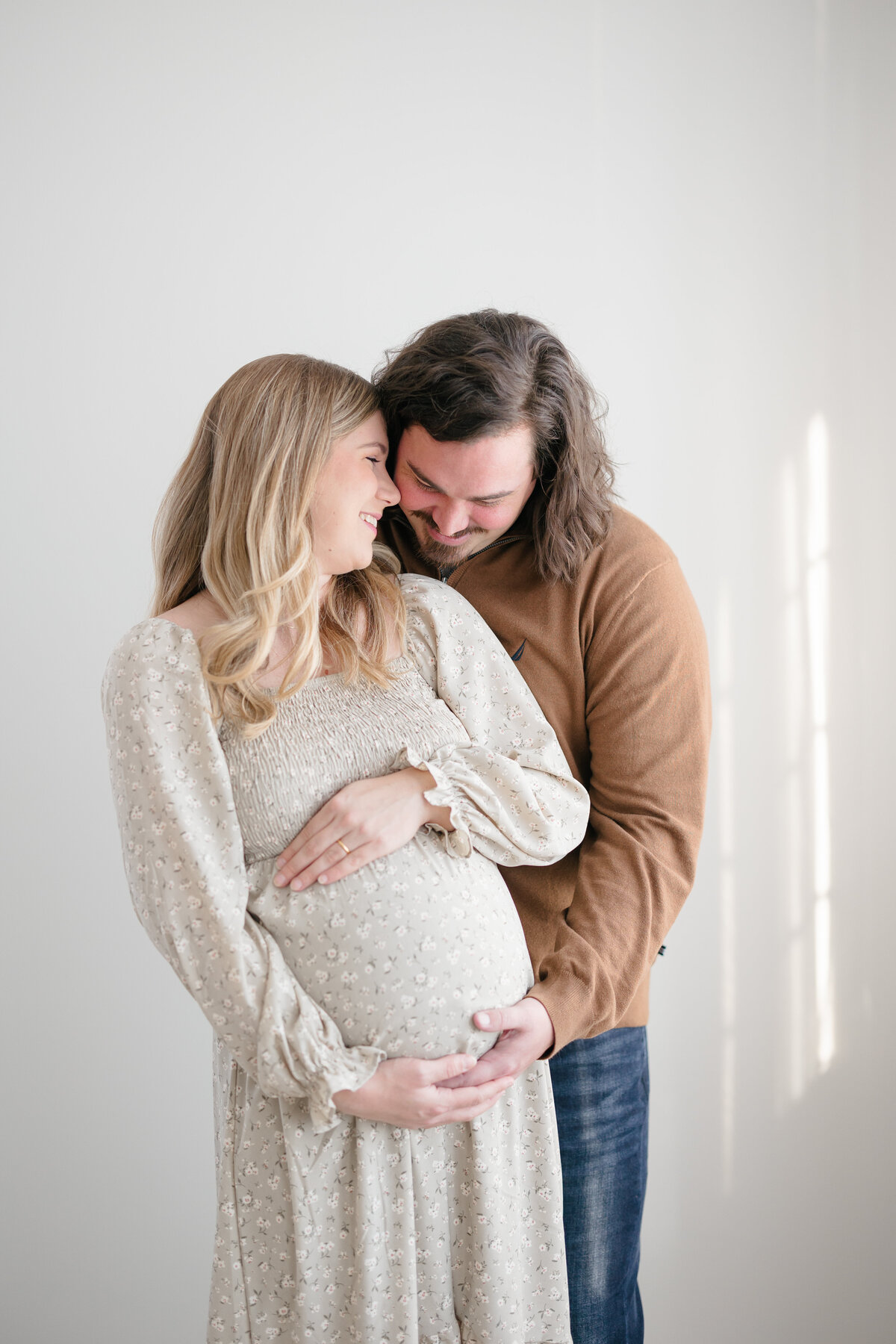 Expecting mom and dad snuggling and smiling as they both embrace mom's growing belly