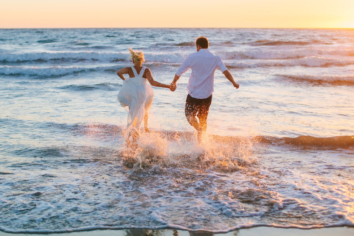 bride and groom run into the ocean during sunset