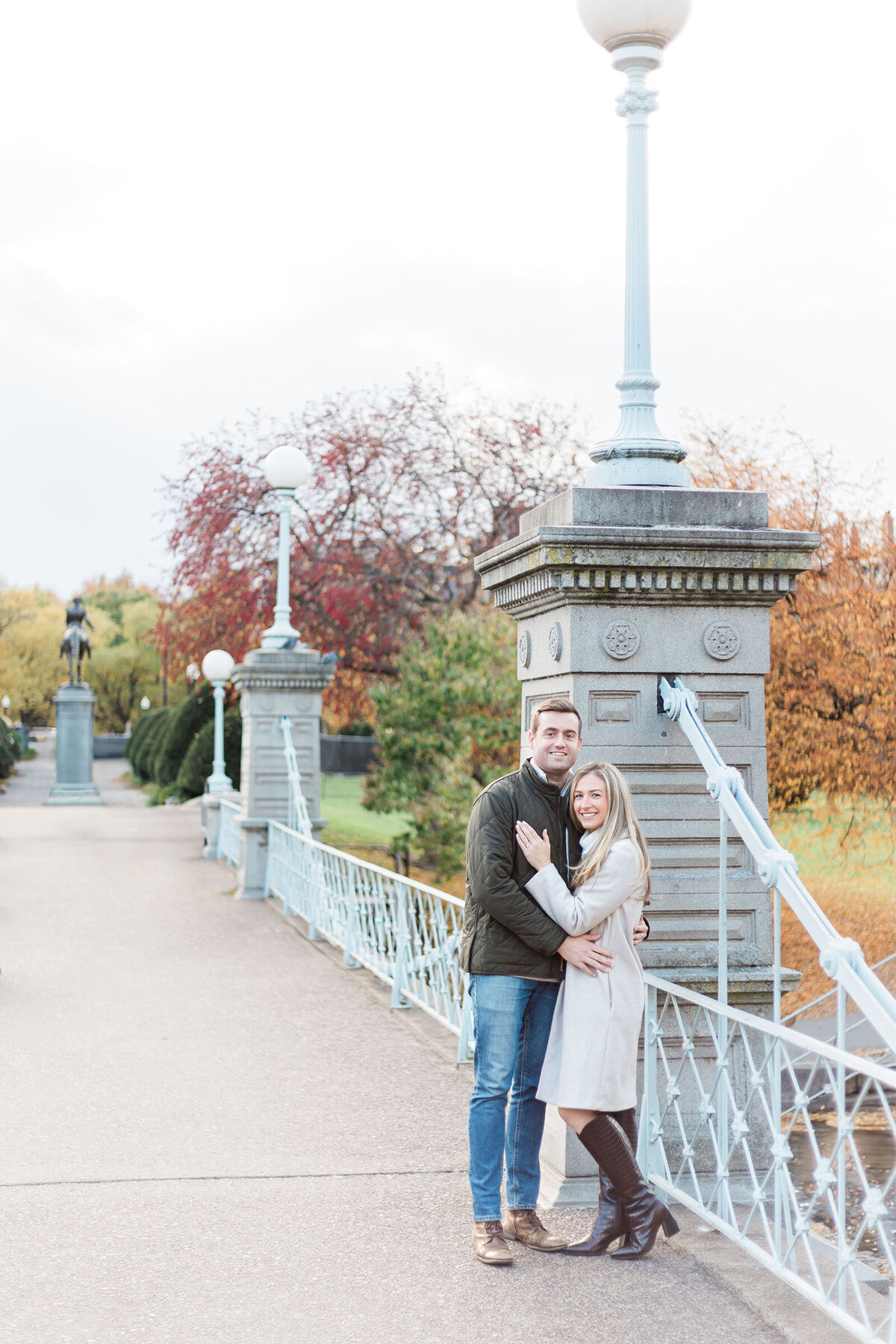 An engaged couple stands on the bridge in the Boston Public Gardens