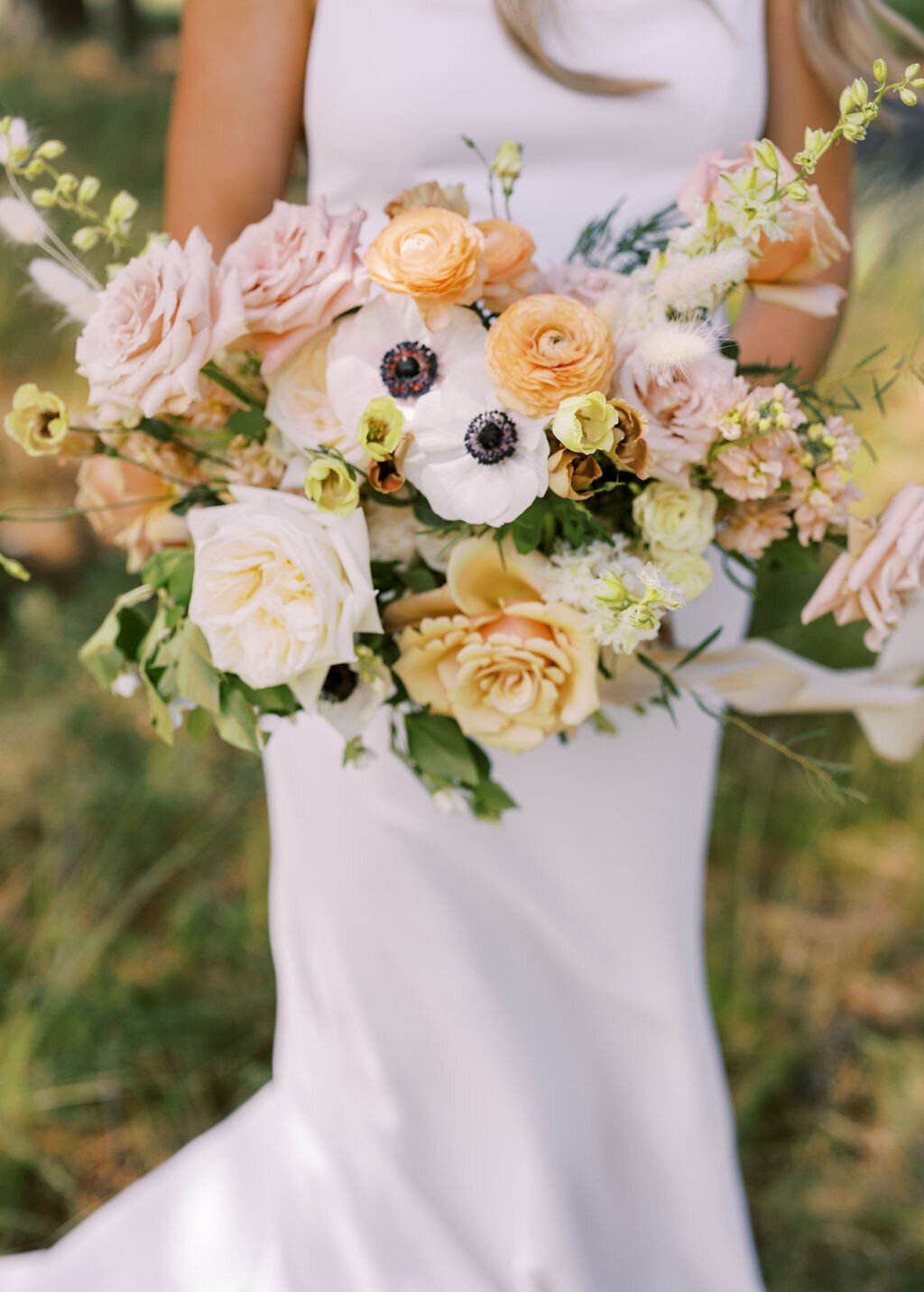 Bride holding a wedding bouquet of pastel anemone, garden roses and ranunculus