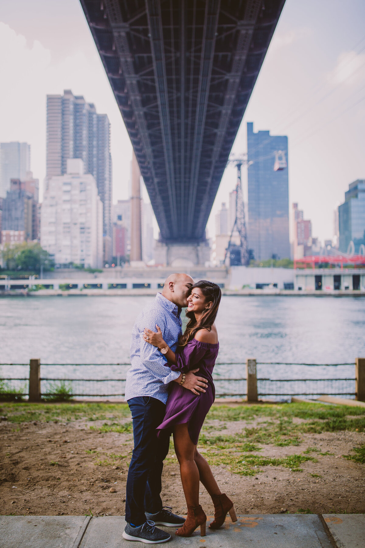 An engaged couple standing under the 59th st queensboro bridge at roosevelt island