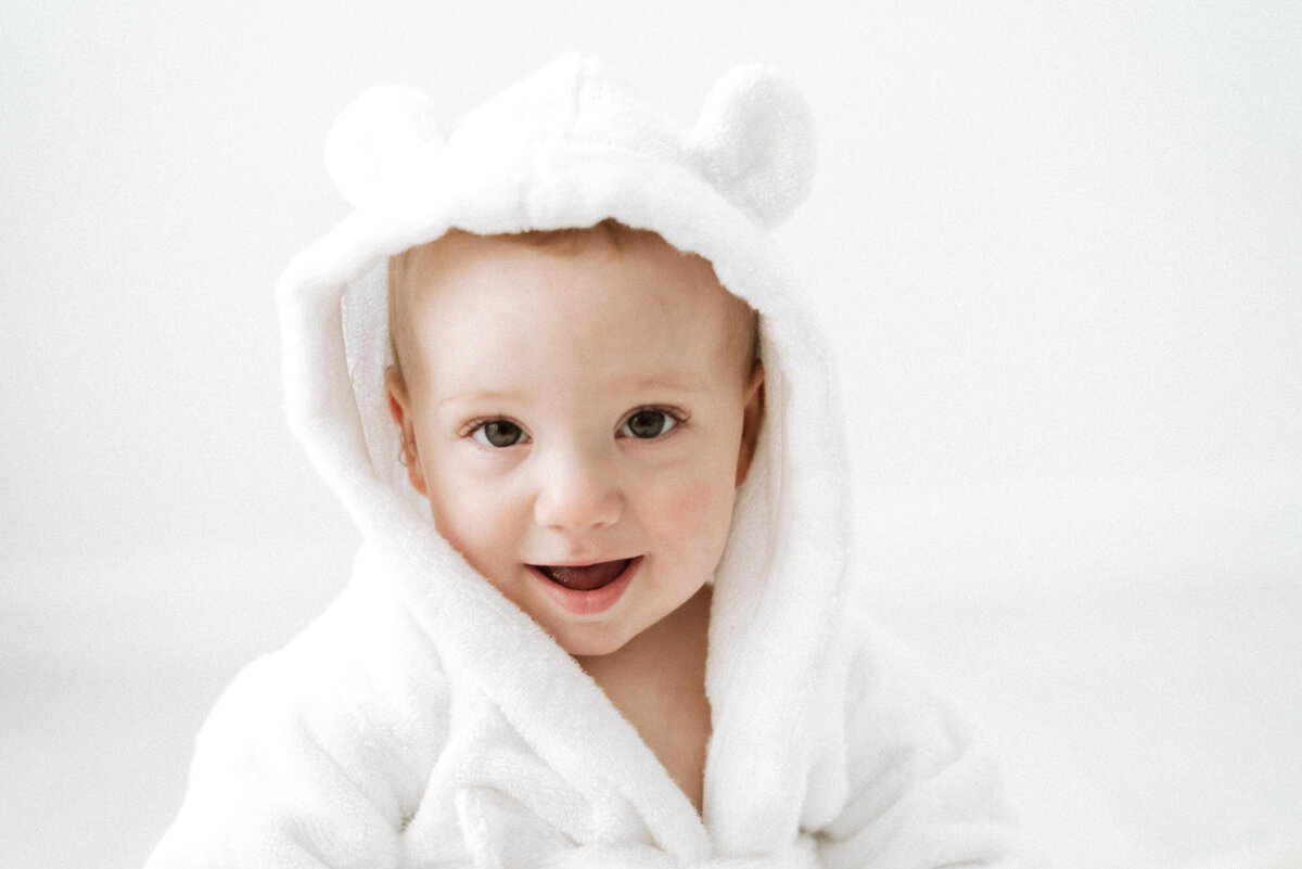 Baby in a white dressing gown smiling at billingshurst cake smash photoshoot