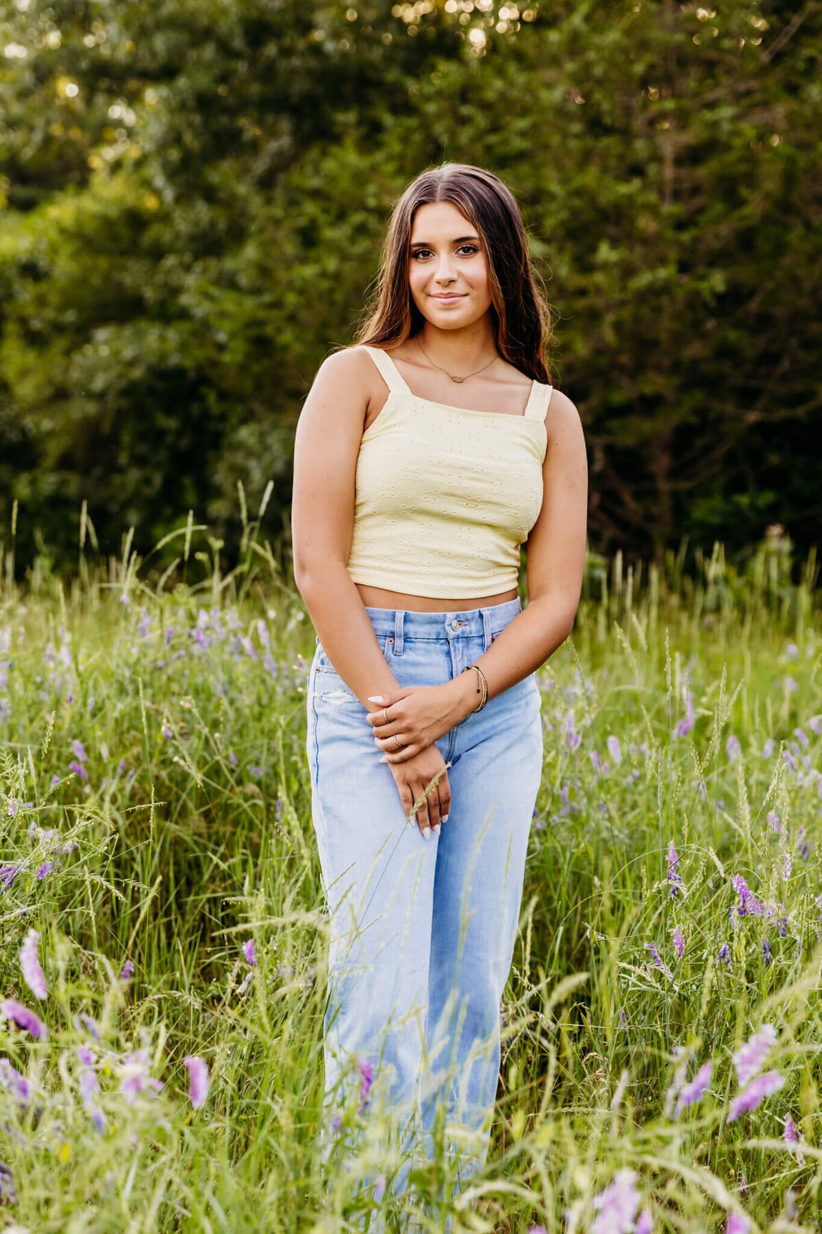 gorgeous teenage girl standing in a flower field and smirking as she holds her arm during her senior photo session