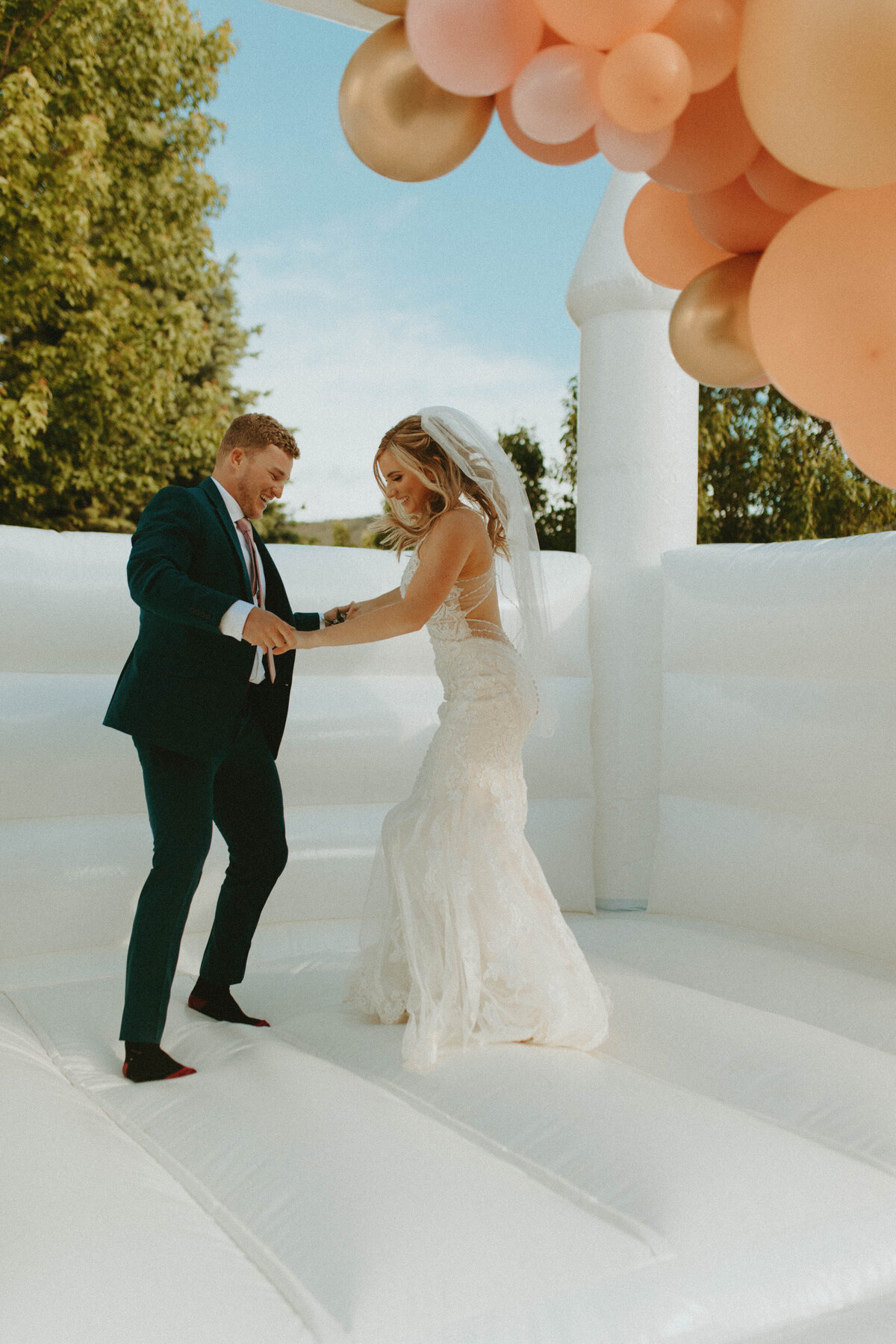 Bride and groom jumping in a white bouncy house.