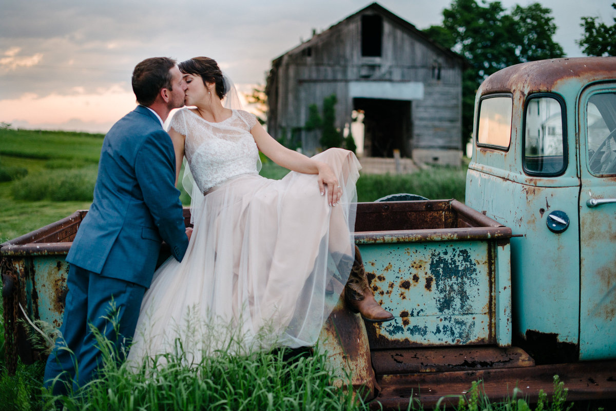 farm wedding bride and groom sitting on vintage truck at sunset