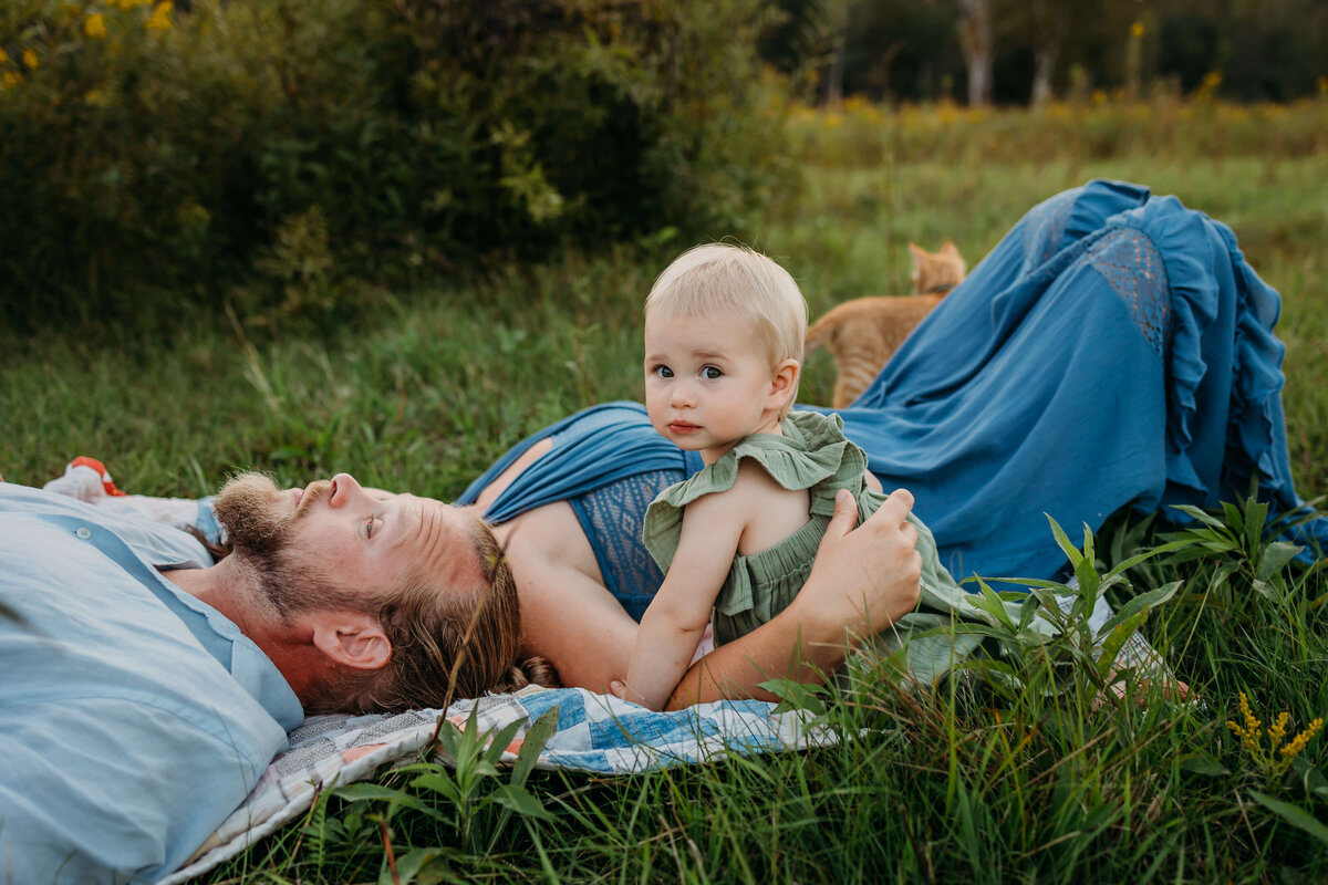 mom and dad laying in grass holding baby