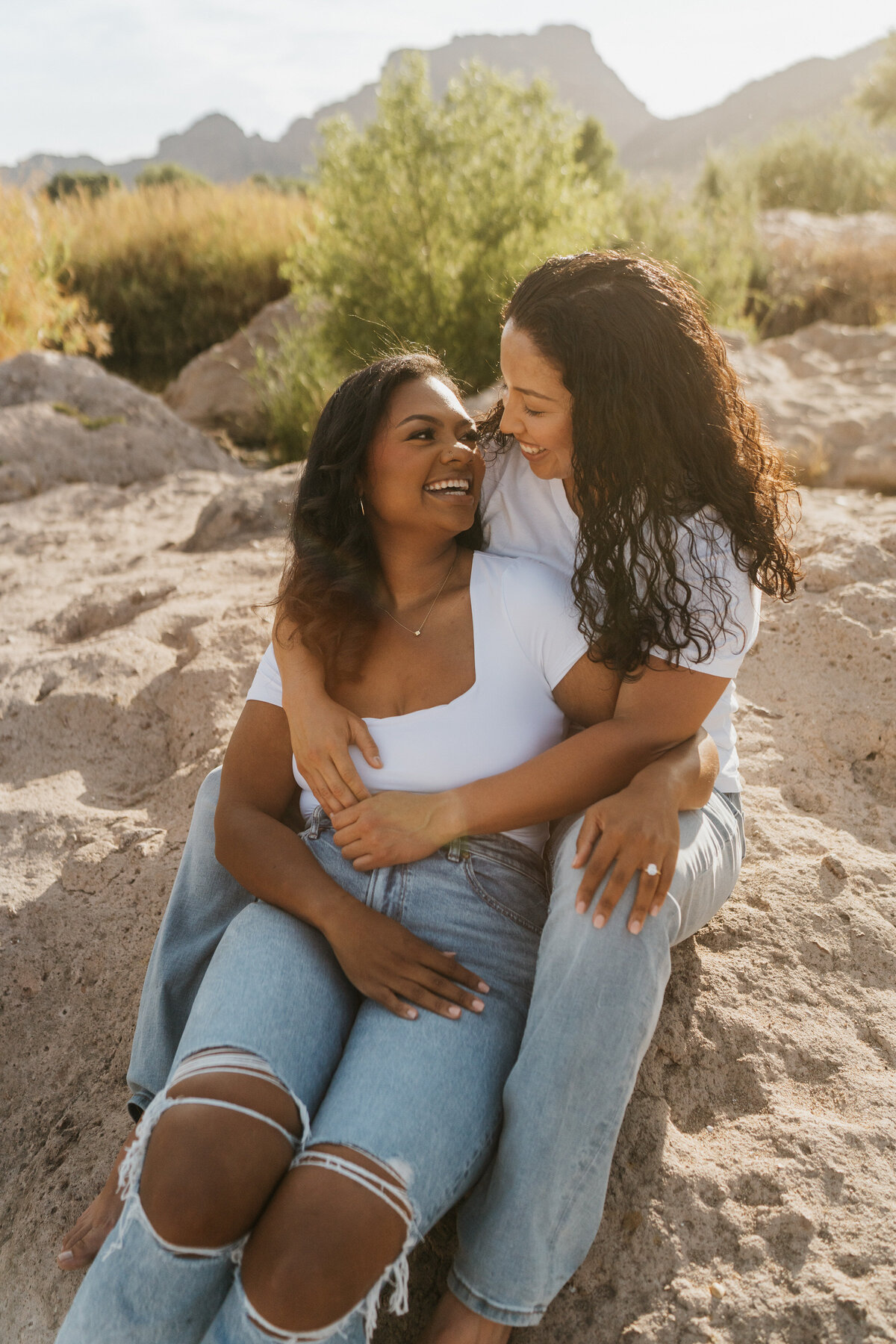 A couple sitting on a rock with their arms around each other smiling