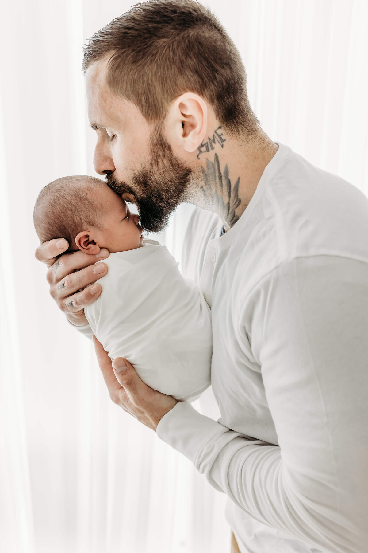 Dad in all white kissing new baby on the head by Luci Levon Photogrpahy