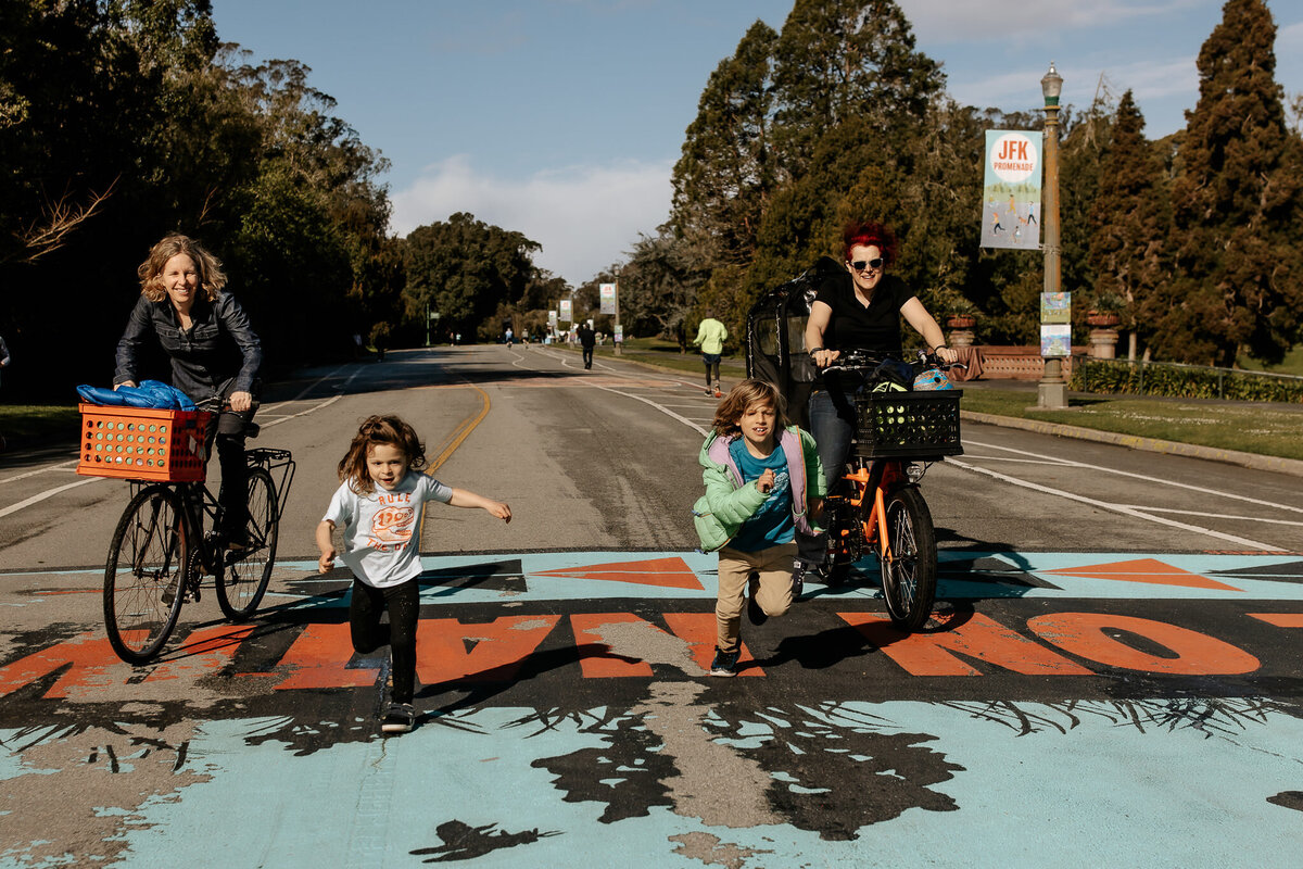 Documentary photo of lesbian moms on bikes with their sons running on JFK Promenade in Golden Gate Park