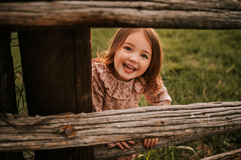 Young girl peeks through fence posts in Boulder, Colorado
