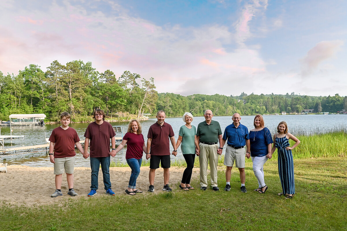 Family stands in a line holding hands in front of a lake